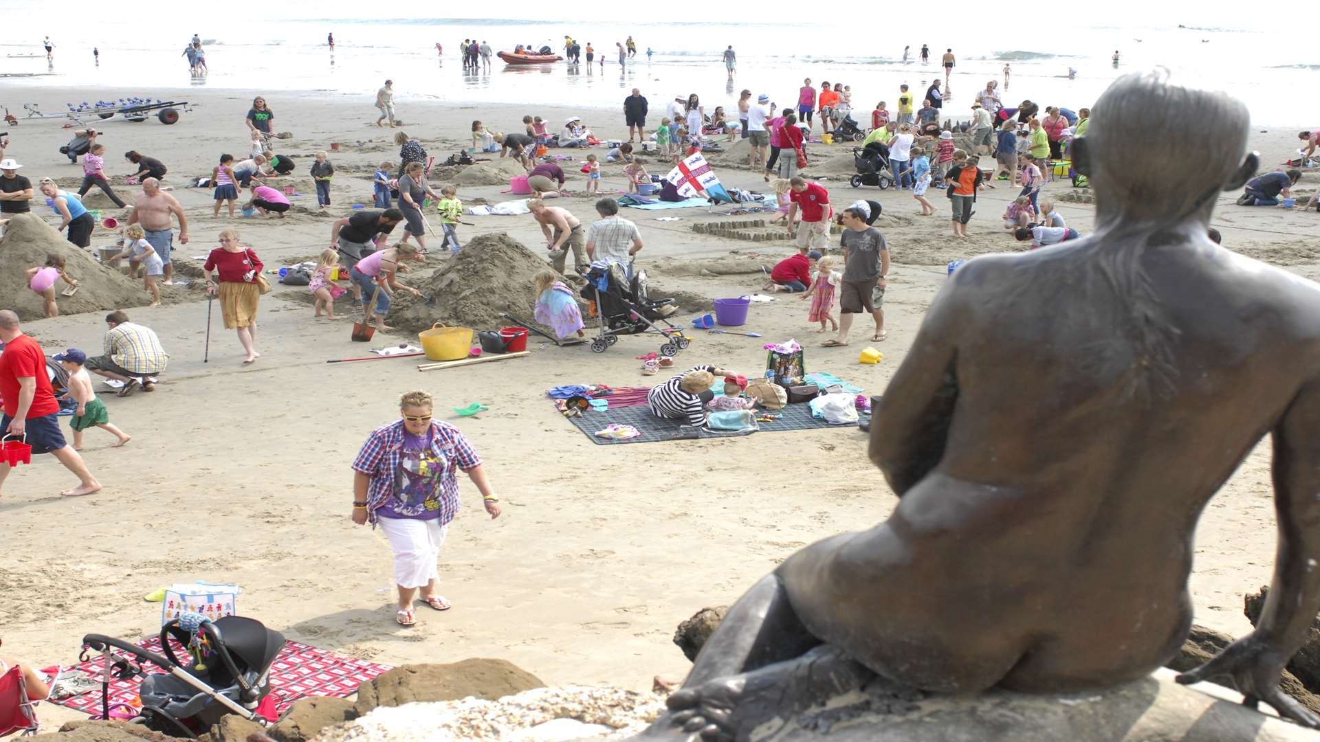 A busy Sunny Sands beach in Folkestone overlooked by Cornelia Parker's permanent Triennial exhibit the Folkestone Mermaid